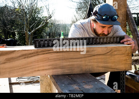 Mann, der Baseball Cap auf Baustelle, messen Holzbalken mit Metall Lineal. Stockfoto