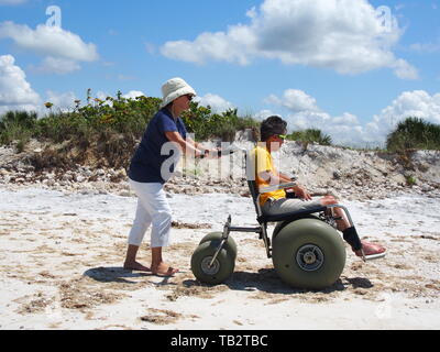 Behinderte Frau in Strandrollstuhl geniesst die Sonne und Sand auf Honeymoon Island State Park in Dunedin, Florida, USA, 10. Mai 2019, © katharine Andrioti Stockfoto