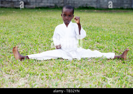 Little boy Kämpfen im Karate Outfit sitzen und mit Kampfkunst Geste im Park Stockfoto