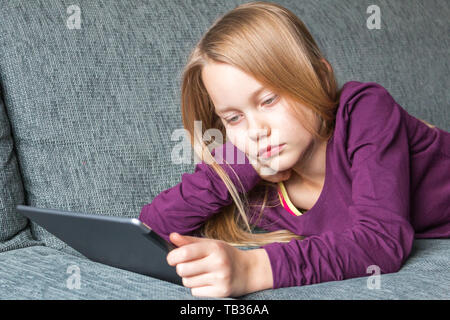 Ein Mädchen liegt auf dem Sofa mit einem Tablet-PC in Ihren Händen Stockfoto