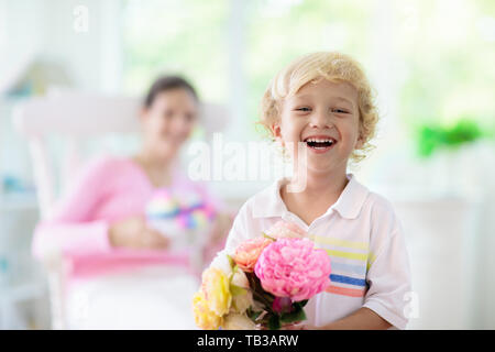 Happy Mother's Day. Kind mit Gegenwart und Blumen für Mama. Little boy Holding verpackte Geschenk und Blumenstrauß für die Mutter. Familie feiern Feder h Stockfoto