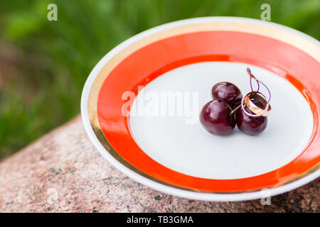 Trauringe und Kirschen. Das Konzept einer Hochzeit. Goldene Ringe Nahaufnahme mit Kirschen Beeren wie Hintergrund. Der leere Raum für Text. Einladungskarte Stockfoto