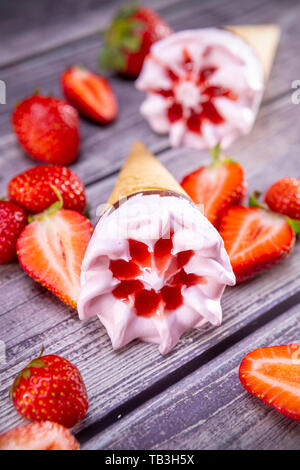 Eistüten mit Erdbeeren auf einem alten Holztisch Sommer. Fokus auf Eis. Stockfoto