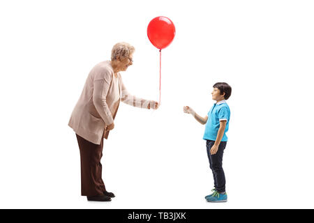 Volle Länge Profil Schuß einer Großmutter, die ein roter Ballon zu einem Enkel auf weißem Hintergrund Stockfoto