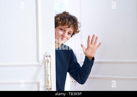 Wenig kaukasischen Jungen öffnet Tür und Wellen hand Hallo Stockfoto