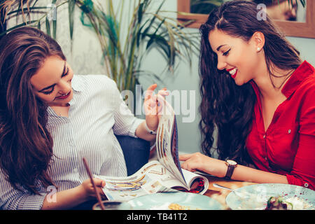 Zwei schöne junge Frauen, die mit Kuchen beim Lesen Magazin im Cafe. - Bild Stockfoto