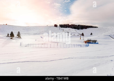 Verschneite Skipisten und eine leere Sessellift in den Alpen bei Sonnenuntergang Stockfoto