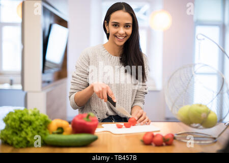 Die junge Frau schneidet Gemüse in der Küche mit einem Messer und Laptop auf dem Tisch. Salat. Diät. Diät Konzept. Gesunde Lebensweise. Cookin Stockfoto