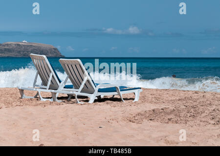 Zwei leere Liegestühle an einem einsamen Sandstrand am Meer. Stockfoto