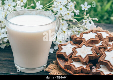 Neben dem Cookies und kleinen weissen Blüten ist ein Glas Tasse Milch auf eine Serviette. Stockfoto