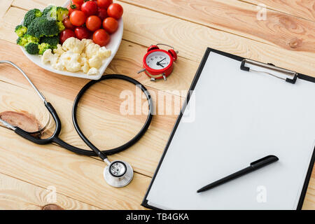 Leere Zwischenablage mit Stift in der Nähe von Stethoskop, Wecker und lecker Gemüse auf Herz-form Platte Stockfoto