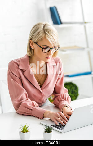 Blonde junge Freiberufler in Gläser mit der Eingabe auf Laptop Stockfoto