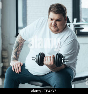 Übergewicht tätowierten Mann sitzt und Trainieren mit hantel im Sportzentrum Stockfoto