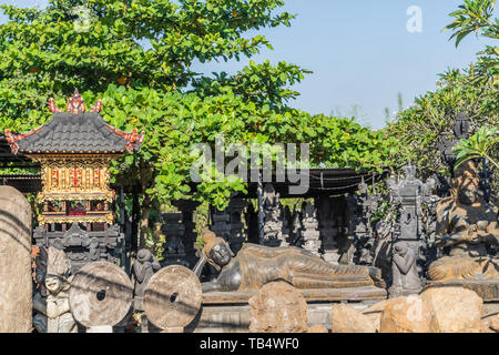 Denpasar, Bali, Indonesien - 26. Februar 2019: religiöse Statuen shop entlang By Pass Ngurah Rai Straße. Liegender Buddha und anderen Statuen unter Baum Folia Stockfoto