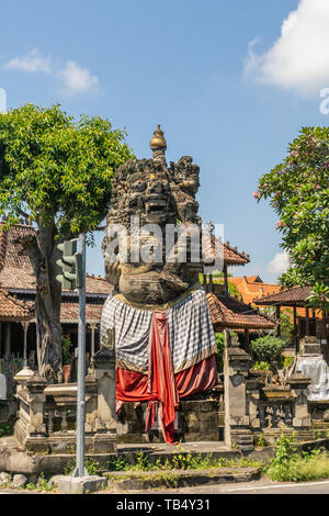 Banjar Gelulung, Bali, Indonesien - 26. Februar 2019: Groß braun Stein Statue von Monster mit rotem drapiert und kariert Grau am Schnittpunkt von Ji Raya Stockfoto
