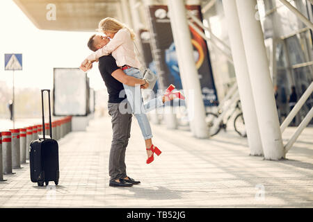 Paar in einem Flughafen. Schöne Blondine in einem weißen Mantel. Mann in einem schwarzen T-Shirt Stockfoto