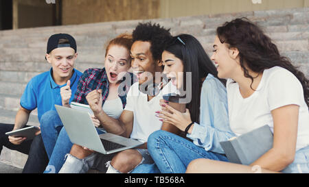 Emotionale Teenage Studenten aufgeregt in Laptop, draußen auf dem Campus Treppen, Panorama Stockfoto