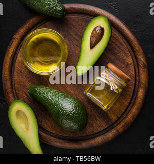 Hälften und ganze Avocados und Öl auf Holzplatte, Ansicht von oben. Gesunde Ernährung Konzept Stockfoto