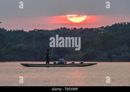 Die Sonne über dem Cuyabeno Wildlife Reserve in Amazonas Ecuador und die lokale Bevölkerung in einem Boot beobachten und Fisch. Stockfoto