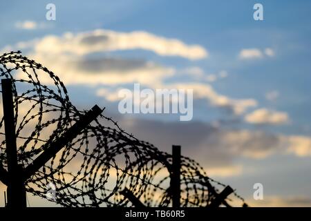 Stacheldraht zaun an der Grenze der EU während des Sonnenuntergangs. Sonnenuntergang hinter dem Stacheldraht. Stockfoto