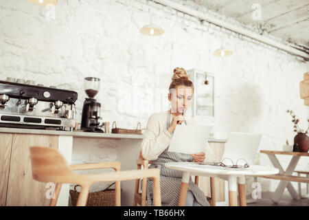 Etwas schief ging. Schöne business Frau am Blatt Papier mit Berechnungen am Laptop arbeiten Suchen umgekippt. Stockfoto