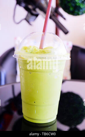 Eistee grüner Tee Milchschaum in Plastikbecher Smoothie frappe Matcha grüner Tee latte und Stroh auf dem Tisch im Café Stockfoto