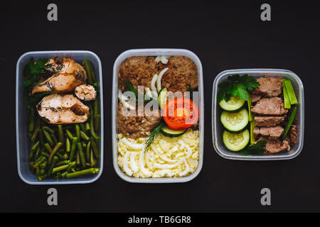 Die gesunde Ernährung in den Containern auf schwarzem Hintergrund: Snack, Abendessen, Mittagessen. Gebackener Fisch, Bohnen, Fleisch Schnitzel, Kartoffeln, Fleisch und Gemüse, Stockfoto