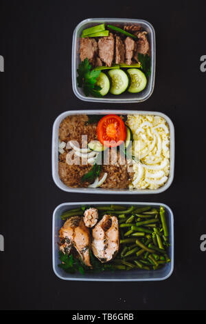 Die gesunde Ernährung in den Containern auf schwarzem Hintergrund: Snack, Abendessen, Mittagessen. Gebackener Fisch, Bohnen, Fleisch Schnitzel, Kartoffeln, Fleisch und Gemüse, Stockfoto