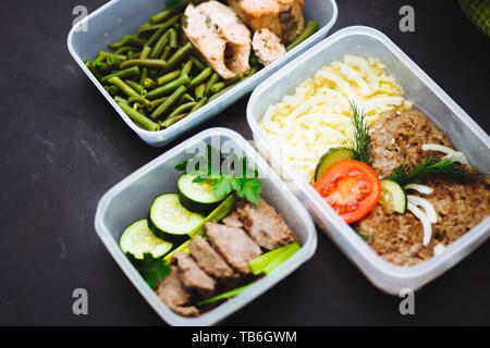 Die gesunde Ernährung in den Containern auf schwarzem Hintergrund: Snack, Abendessen, Mittagessen. Gebackener Fisch, Bohnen, Fleisch Schnitzel, Kartoffeln, Fleisch und Gemüse, Stockfoto