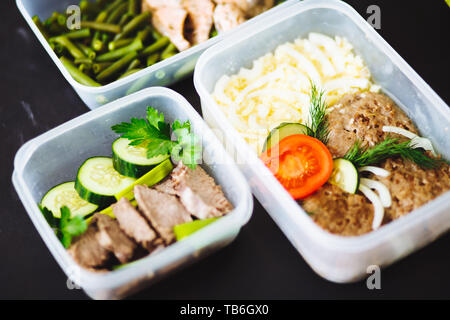Die gesunde Ernährung in den Containern auf schwarzem Hintergrund: Snack, Abendessen, Mittagessen. Gebackener Fisch, Bohnen, Fleisch Schnitzel, Kartoffeln, Fleisch und Gemüse, Stockfoto