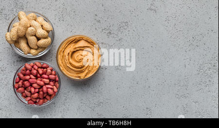 Peanut Butter und Erdnüsse in drei Schalen auf konkreten Hintergrund, Ansicht von oben, kopieren Raum Stockfoto