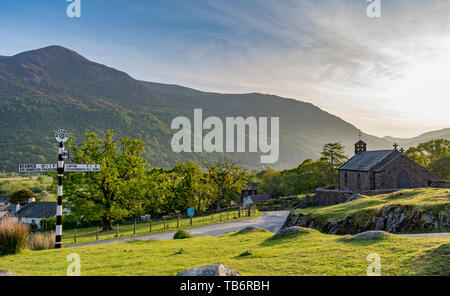 St. Jame's Kirche Buttermere Lake District, Cumbria Uk in der Abendsonne mit dem Schwarzen und Weißen fingerpost mit lokalen Richtungen Stockfoto