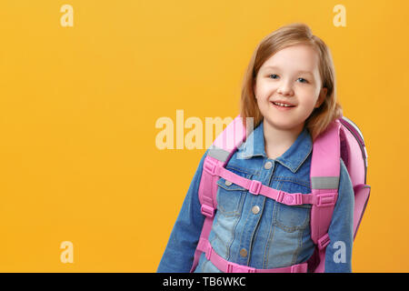 Porträt von einem kleinen Mädchen Schülerin mit einem Rucksack auf gelbem Hintergrund. Das Kind in der Nähe. Zurück zu Schule. Der Begriff der Bildung. Stockfoto