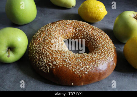 Eine frische Bagel mit Sesam. In der Nähe befinden sich Obst - Äpfel und Zitronen. Auf einem vintage Hintergrund. Leckeres und gesundes Frühstück. Stockfoto