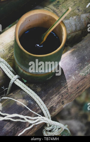 Frische bio Bambus Tasse und Löffel mit heißem köstlicher Kaffee auf einer Bank im Dschungel in Thailand gefüllt. Ökotourismus Stockfoto