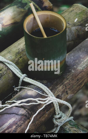 Frische bio Bambus Tasse und Löffel mit heißem köstlicher Kaffee auf einer Bank im Dschungel in Thailand gefüllt. Ökotourismus Stockfoto