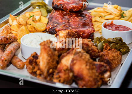 Schüssel gemischter Aufschnitt. Gegrillte Spareribs, Chicken Wings und Würstchen mit Pommes frites Stockfoto