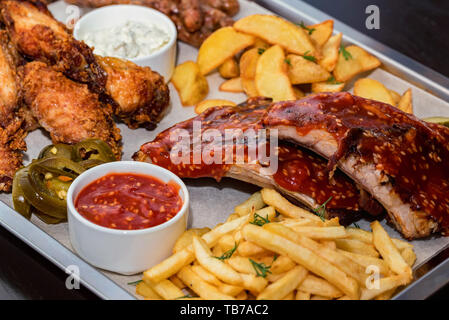 Schüssel gemischter Aufschnitt. Gegrillte Spareribs, Chicken Wings und Würstchen mit Pommes frites Stockfoto
