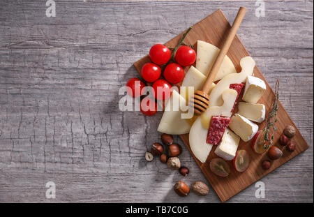Holzbrett mit Auswahl an leckeren Käse, Tomaten und Honig auf Tisch Stockfoto