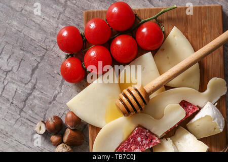 Holzbrett mit Auswahl an leckeren Käse, Tomaten und Honig auf Tisch Stockfoto