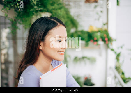 Junge schöne Frau sitzt und liest ein Buch auf der Terrasse Stockfoto