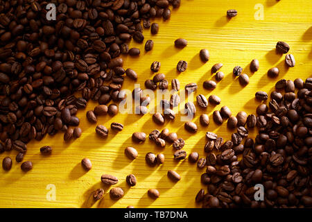 Geröstete Kaffeebohnen in Haufen angeordnet auf zwei gegenüberliegenden Ecken in einer Diagonalen bunt gelb Holz gesehen von oben Stockfoto