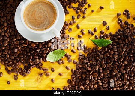 Tasse schaumigen Cappuccino mit gerösteten Bohnen organisiert in zwei Ecken mit Streifen diagonal gelb Holz Hintergrund sichtbar zwischen Stockfoto