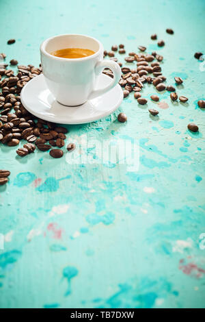 Tasse starken frisch gebrühtem Espresso mit verstreuten gerösteten Bohnen auf einem strukturierten blaue Farbe Hintergrund mit Spritzern und Platz kopieren Stockfoto