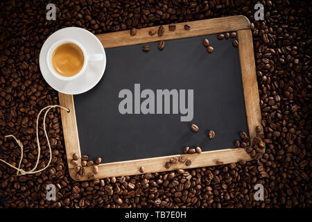 Alte Schule Schiefer mit leeren Kopie Raum umgeben mit gerösteten Kaffeebohnen mit einer kleinen Tasse heißen schaumigen Espresso ruht auf dem Frame in einem overhea Stockfoto