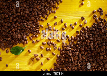 Frisch geröstete Kaffeebohnen in gegenüberliegenden Ecken mit diagonalen Linie zwischen auf gelbem Hintergrund Holz in einer Ansicht von oben Stockfoto