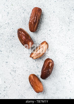 Süße raw Termine auf grauzement Hintergrund. Ganze Termine und Hälfte mit Knochen Datum auf grauem Beton Oberfläche. Zucker freie Alternativen konzept mit Platz für Text. Ansicht von oben oder flach-legen. Vertikale. Stockfoto