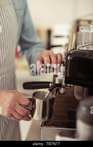 Aufschäumen der Milch. Hände von barista Aufschäumen der Milch für den Kaffee in der Nähe der Kaffeemaschine. Stockfoto