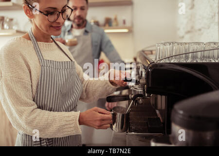 Schönen job. Lächelnde Frau, die von der schwarzen Kaffee Maschine und Aufschäumen der Milch in den Krug. Stockfoto