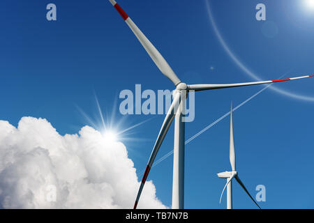 Zwei Windenergieanlagen auf einen blauen Himmel mit Wolken und Sonnenstrahlen - Erneuerbare Energie Konzept Stockfoto